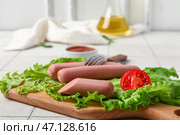 Доска вкусных колбасок с листьями салата и помидорами на белом плиточном фоне. Стоковое фото, фотограф Pixel_shot / Фотобанк Лори