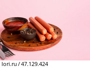 Тарелка с вкусными сосисками и миска с кетчупом на розовом фоне. Стоковое фото, фотограф Pixel_shot / Фотобанк Лори