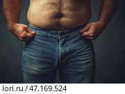 An overweight man trying to button or pull up his jeans. His bare belly with thick hair clearly protrudes above his waistband, and his hands are holding the edges of his jeans tightly, indicating their tightness. The atmosphere of the photo conveys the struggle with excess weight and physical discomfort, and the play of light emphasizes the texture of the skin, hair and fabric. Стоковое AI-изображение, AI-художник Анна Кривицкая / Фотобанк Лори