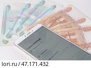 Смартфон с открытым банковским приложением -  личным кабинетом самозанятого (плательщиков налога на профессиональный доход) на фоне пятитысячных и тысячных  купюр. Стоковое фото, фотограф Snezka / Фотобанк Лори