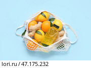 Сетчатый мешок с свежими лимонами, апельсинами, имбирем и бутылкой соков на голубом фоне. Стоковое фото, фотограф Pixel_shot / Фотобанк Лори
