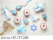 Композиция Хануки с пончиками, крутилками, менорой и подарочными коробками на белом деревянном фоне. Стоковое фото, фотограф Pixel_shot / Фотобанк Лори