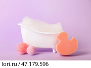 Маленькая ванна с пеной, губкой и бомбами для ванны на лиловом фоне. Стоковое фото, фотограф Pixel_shot / Фотобанк Лори