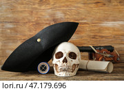 Человеческий череп в пиратской шляпе, игрушечная пушка, компас и свиток на коричневом деревянном фоне. Стоковое фото, фотограф Pixel_shot / Фотобанк Лори