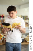 Casually dressed young guy examining two chip bags while shopping for snacks in local grocery store, comparing ingredients and nutritious value before buying. Стоковое видео, видеограф Яков Филимонов / Фотобанк Лори