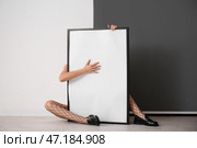 Женщина в колготках в сеточку с пустой рамкой сидит у черно-белой стены. Стоковое фото, фотограф Pixel_shot / Фотобанк Лори