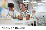 Young couple joyfully talking and working together on ceramic pottery, enjoying creative process while painting mugs in light workshop. Стоковое видео, видеограф Яков Филимонов / Фотобанк Лори