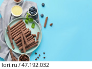 Композиция с вкусными шоколадными вафельными трубочками, черникой, кофейными зернами, сгущенным молоком и мятой на синем фоне. Стоковое фото, фотограф Pixel_shot / Фотобанк Лори