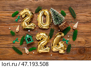 Композиция с фигурой 2024 из фольгированных воздушных шаров, новогодними украшениями и ветками ели на деревянном фоне. Стоковое фото, фотограф Pixel_shot / Фотобанк Лори