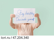 Пожилая женщина держит плакат с текстом ОСТАВАЙТЕСЬ ЗДОРОВЫМ - ВАКЦИНИРУЙТЕ СЕБЯ на цветном фоне. Стоковое фото, фотограф Pixel_shot / Фотобанк Лори