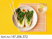 Тарелка вкусной тушеной капусты пак-чой с соевым соусом и стаканом воды на желтом фоне. Стоковое фото, фотограф Pixel_shot / Фотобанк Лори