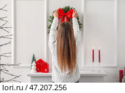 Молодая женщина вешает рождественский венок на светлую стену в гостиной. Стоковое фото, фотограф Pixel_shot / Фотобанк Лори