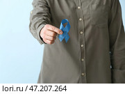 Человек с голубой лентой на цветном фоне, крупным планом. Концепция рака толстой кишки. Стоковое фото, фотограф Pixel_shot / Фотобанк Лори