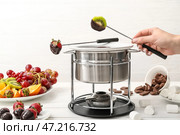 Женщина, окуная вкусные фрукты в миску с шоколадным фондю на столе. Стоковое фото, фотограф Pixel_shot / Фотобанк Лори