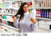 Adult Latina choosing haircare cosmetics in specialized boutique. Стоковое фото, фотограф Яков Филимонов / Фотобанк Лори