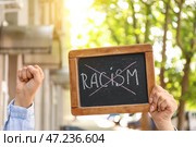 Женщина держит классную доску с перечеркнутым словом РАСИЗМ на открытом воздухе. Стоковое фото, фотограф Pixel_shot / Фотобанк Лори