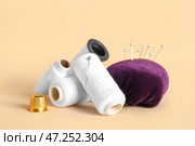 Катушки с нитками, наперсток и игольница с шариковыми штифтами на цветном фоне. Стоковое фото, фотограф Pixel_shot / Фотобанк Лори