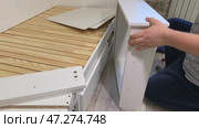The man is assembling pull-out shelves for the sofa bed. He joins and secures them using furniture cam locks. Стоковое видео, видеограф Vadzim Yakubovich / Фотобанк Лори