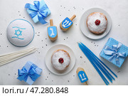 Тарелки с пончиками, еврейская шляпа, дрейделы, свечи и подарки для празднования Хануки на белом фоне. Стоковое фото, фотограф Pixel_shot / Фотобанк Лори