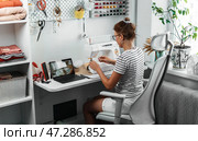 Seamstress enjoys working in well-organized sewing studio, surrounded by tools and materials. Comfortable environment enhances creativity and productivity in tailoring business. Стоковое фото, фотограф Енваев Андрей / Фотобанк Лори