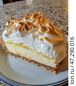 A slice of Lemon Meringue Pie. It's made up of three layers: a crisp shortbread base, a rich, rich lemon curd, and an airy meringue layer that's toasted to golden peaks. The pie is delicious, with a light texture and a pleasant combination of sweet and sour. The backdrop is a marble countertop, and the slice sits on a white plate with a thin blue border. Стоковое AI-изображение, AI-художник Анна Кривицкая / Фотобанк Лори
