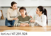 Sad woman sits silently in kitchen, adult girls sympathize and comfort her. Стоковое фото, фотограф Яков Филимонов / Фотобанк Лори