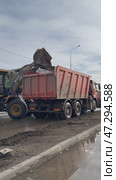 ANGARSK, IRKUTSK REGION, RUSSIA - March 20, 2025: Vertical video of spring cleaning of city roads. A backhoe loader unloads icy mud from the road into a dump truck for removal. Редакционное видео, видеограф Виктория Катьянова / Фотобанк Лори