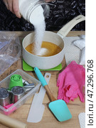 A woman adds sugar to apple juice in a saucepan. She is preparing syrup for homemade marshmallows. Zefir-making tools are nearby on the table. Стоковое фото, фотограф Vadzim Yakubovich / Фотобанк Лори