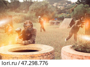 Paintball players of one team in camouflages and masks aiming with gun in shootout playing. Стоковое фото, фотограф Яков Филимонов / Фотобанк Лори