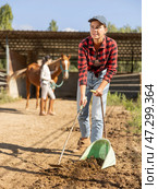 Smiling girl worker scoops horse droppings into shovel and cleans up cattle. Стоковое фото, фотограф Яков Филимонов / Фотобанк Лори