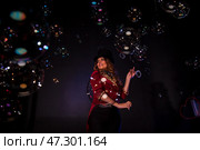 Captivating audience members, a woman magician dazzles with her extraordinary soap bubble show. Clad in vibrant theatrical garb, she masterfully conjures bubbles amidst a magical ambiance. Стоковое фото, фотограф Aleksandr Golubev / Фотобанк Лори