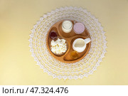 Flat lay of four types of organic dairy products - cottage cheese, yogurt, milk and sour cream on a wooden plate on a handmade lace napkin. Delicious and healthy breakfast. Healthy lifestyle. Стоковое фото, фотограф Виктория Катьянова / Фотобанк Лори