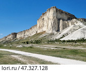 The majestic White Rock (Ak-Kaya), located in Crimea, near the town of Belogorsk. This is one of the most recognizable and picturesque natural wonders of the peninsula. Snow-white limestone cliffs rise above the steppe valley, creating a contrast between the bright blue sky, dry grasses and light rocks. The rock looks monumental, as if it keeps ancient secrets - it really has archaeological and historical significance.White Rock (Ak-Kaya) is a limestone cliff about 100 meters high, formed in the Cretaceous period. This is a place of archaeological finds, legends, filming and inspiration for artists and poets. Стоковое фото, фотограф Анна Кривицкая / Фотобанк Лори