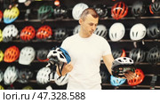 Focused interested male cyclist choosing new bicycle helmet in sports store specializing in cycling gear, comparing design and safety features of two models. Стоковое видео, видеограф Яков Филимонов / Фотобанк Лори