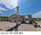 Ancient ruins on the territory of Chersonesos Taurica in Crimea. In the foreground is a rectangular square with preserved marble columns and an arch-gate in the center. These architectural elements are reminiscent of the greatness of the ancient civilization. Beyond the ruins stretches a green area and a blue sky with light clouds. All together creates an atmosphere of peace, light and deep historical significance. (2021 год). Стоковое фото, фотограф Анна Кривицкая / Фотобанк Лори