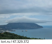 A picturesque view of Gurzuf from above. In the center of the composition is the majestic Mount Ayu-Dag, covered with a thick cap of clouds, like a magic veil. Below is the coast with houses, hotels and a bay in which the famous Adalary rocks are visible, like two guards at the entrance to the sea. Everything is surrounded by dense Crimean forests and greenery, creating a feeling of silence, peace and harmony. The atmosphere is filled with cool freshness, the breath of the sea and the anticipation of something new. Стоковое фото, фотограф Анна Кривицкая / Фотобанк Лори