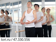 Sports young man in black and white sportswear, training first position of ballet stance at barre with group in choreography studio. Стоковое фото, фотограф Яков Филимонов / Фотобанк Лори