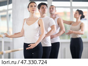 Experience female ballet instructor adjusting students form. Diligent girls and boys practice ballet movements near ballet barre in dancing hall. Стоковое фото, фотограф Яков Филимонов / Фотобанк Лори