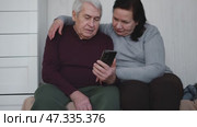 Old couple using a phone together while relaxing in the kitchen at home. Elderly man and woman spending leisure time browsing online with a smartphone. Happy senior married couple typing, learning. Стоковое видео, видеограф Марина Демидюк / Фотобанк Лори