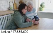 Old couple using a phone together while relaxing in the kitchen at home. Elderly man and woman spending leisure time browsing online with a smartphone. Happy senior married couple typing, learning. Стоковое видео, видеограф Марина Демидюк / Фотобанк Лори