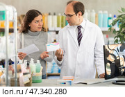 Experienced pharmacist helps girl buy medicine - he reads the prescription and compares it with data on computer. Стоковое фото, фотограф Яков Филимонов / Фотобанк Лори