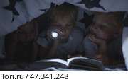 Three young children are reading a book with a flashlight under the covers at night. Стоковое видео, видеограф Mikhail Davidovich / Фотобанк Лори