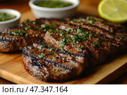 A delicious, juicy steak grilled to perfection, with distinctive grill marks. The meat is sliced ​​and topped with a green sauce, presumably chimichurri - a mixture of parsley, garlic, vinegar and oil. The background is a wooden cutting board, giving the dish a cozy, homey feel. In the background, bowls of sauce and half a lemon are visible, adding a sense of freshness and balance to the flavors. Стоковое AI-изображение, AI-художник Анна Кривицкая / Фотобанк Лори