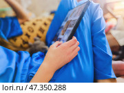 Девушка в синей одежде держит планшет, на экране которого отображаются различные изображения. Он сидит, согнув ноги в коленях, и планшет лежит на коленях. Стоковое фото, фотограф Valeryi Vysotkov / Фотобанк Лори