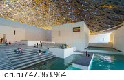 Abu Dhabi, United Arab Emirates - Jan 17 2024, Panoramic view of white concrete buildings and corniche under metal dome of the Louvre Abu Dhabi Museum, at daytime, Abu Dhabi, United Arab Emirates. Редакционное фото, фотограф Сергей Богомяко / Фотобанк Лори