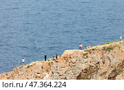 BAIKAL LAKE, OLKHON ISLAND, USYK VILLAGE, IRKUTSK REGION, RUSSIA - August 02, 2024: Group of tourists travel along rocky cape of Sagan-Khushun or Three Brothers and take pictures of scenic views. Редакционное фото, фотограф Виктория Катьянова / Фотобанк Лори
