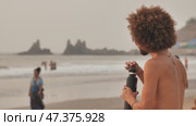 Goa, India - December 12, 2018: A man with a fluffy hairstyle drinks juice on the beach. Редакционное видео, видеограф Mikhail Davidovich / Фотобанк Лори