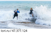 Alanya, Antalya, Türkiye, Turkey - April 05 2023, Two people, a young couple, are taking photos in the waves with sea foam, during a storm, at sunset, the Mediterranean Sea, Alanya, Antalya, Türkiye. Редакционное фото, фотограф Сергей Богомяко / Фотобанк Лори