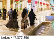 Doha, Qatar - Jan 06 2024, a view of three Arab women walk down the street in the Msheireb district, at night, the street lights are on, Doha, Qatar. Редакционное фото, фотограф Сергей Богомяко / Фотобанк Лори