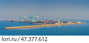 Manama, Bahrain - Jan 08 2024, Panoramic view of Bahrain commercial international  port with blue cranes, pier, buildings and containers, with sea on foreground, at daytime, Manama, Bahrain. Редакционное фото, фотограф Сергей Богомяко / Фотобанк Лори
